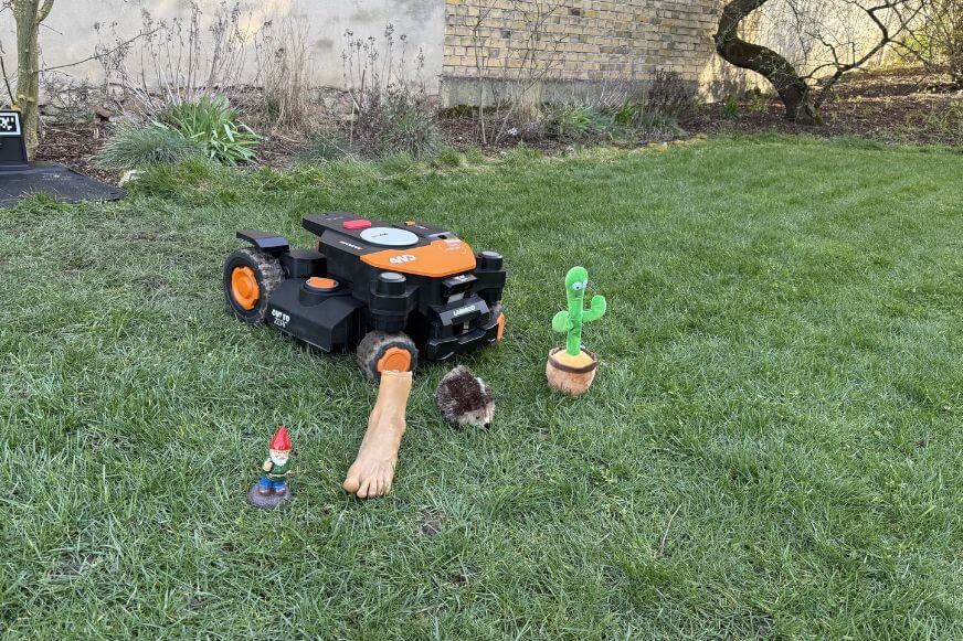 Worx Landroid Vision Cloud 4WD Mähroboter steht vor verschieden großen Hindernissen wie Kaktus, Gartenzwerg, Fuß, Igel im Smart Home Fox Praxistest